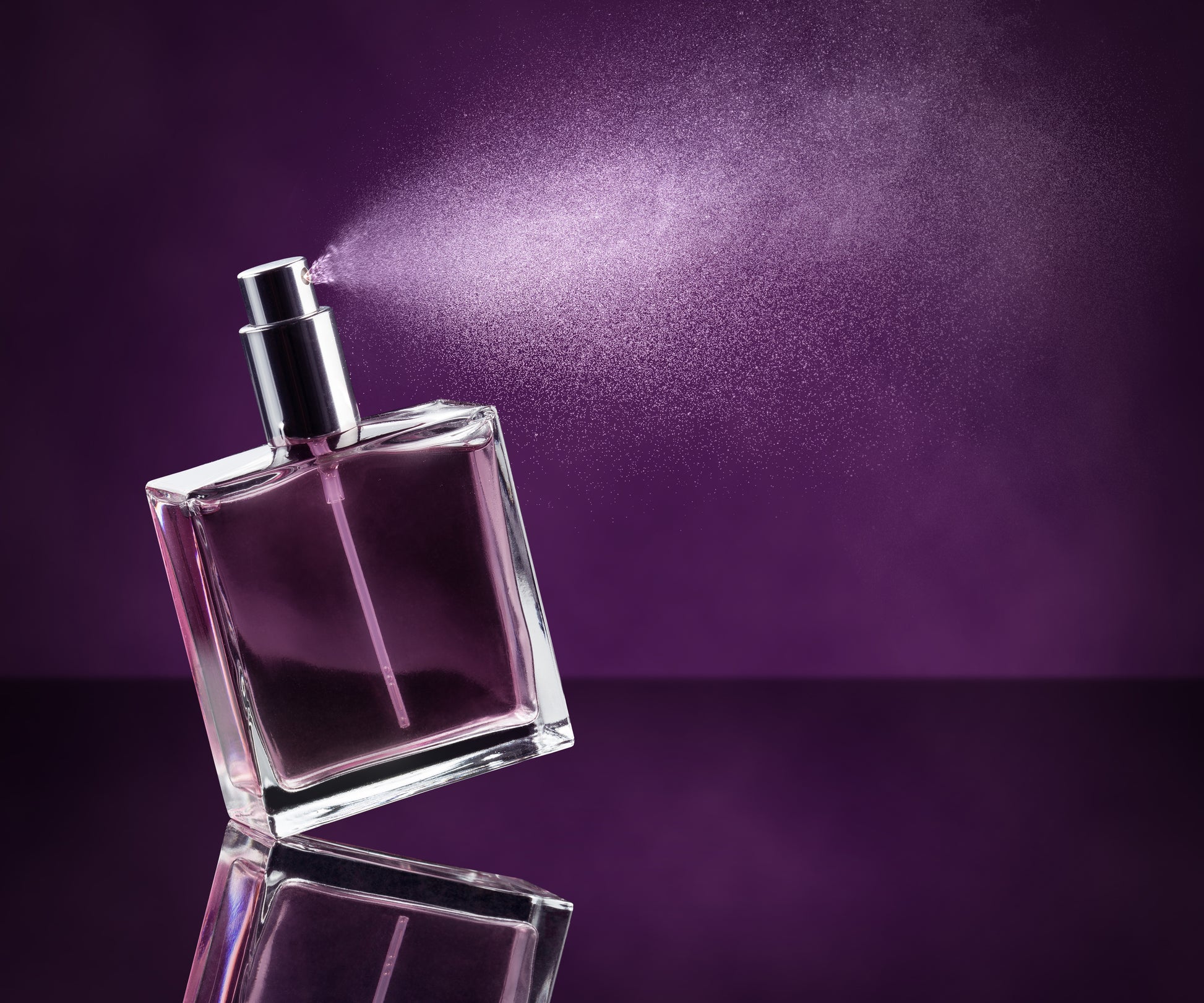 Stock photo of a blank perfume bottle spraying against a deep violet background