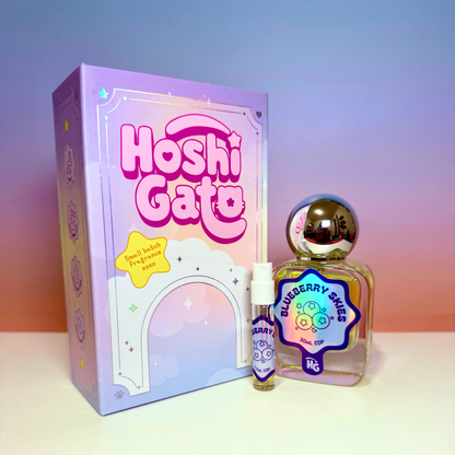 a lavender box, rounded glass bottle labelled "blueberry skies" with a metallic silver cap, a matching sample vial, on a blue and peach gradient background
