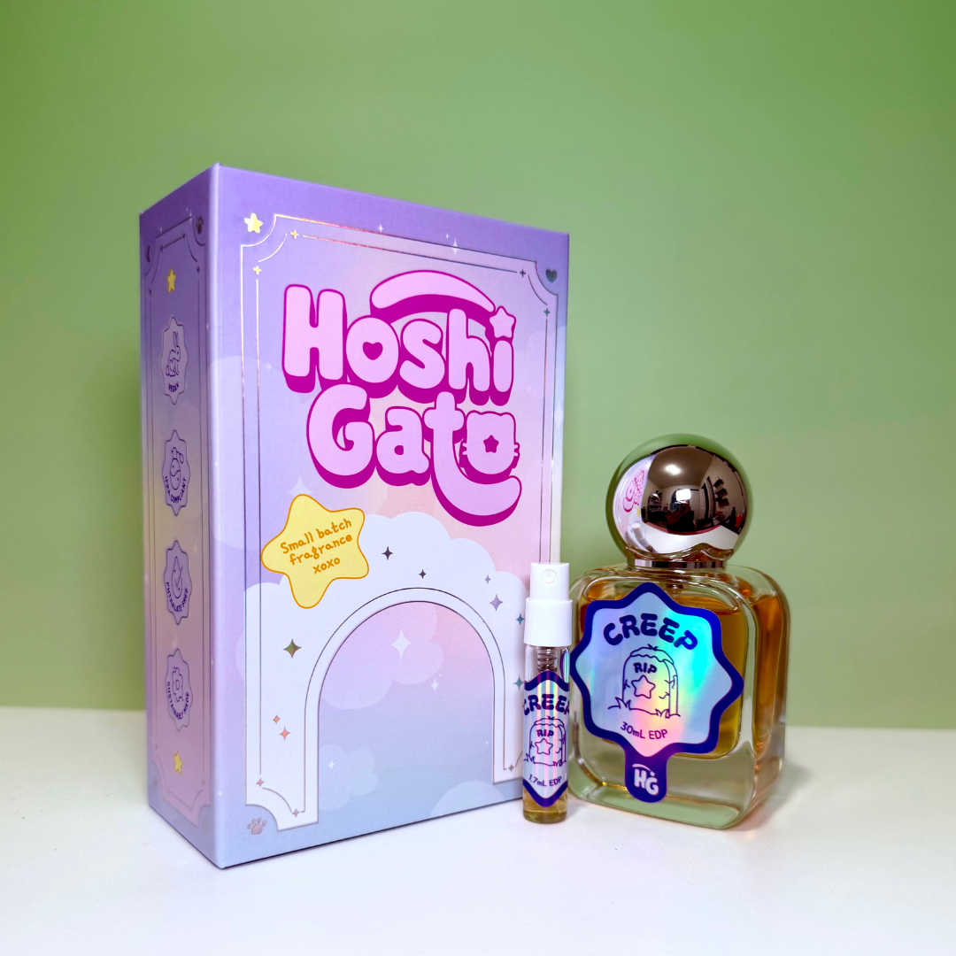 a lavender box, a clear glass bottle of Creep perfume with a rounded silver cap, a matching sample vial, on a light green background.
