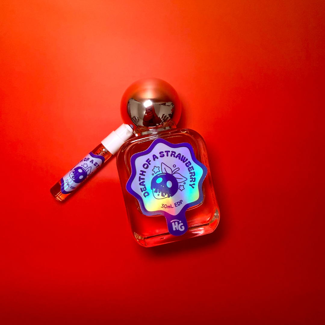 A small perfume bottle labeled 'Death of a Strawberry' with a metallic silver cap, shown next to a matching travel spray vial on a solid red gradient background.