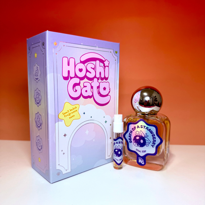 A lavender box labeled 'Hoshi Gato', a small spray bottle, and a larger glass perfume bottle labelled "Death of a strawberry" with a metallic cap, all set against a warm orange gradient background.