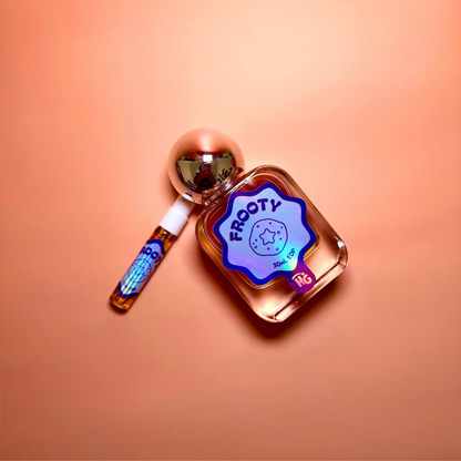 A small frosted glass perfume bottle labeled 'FROOTY' with a metallic silver cap, shown next to a matching amber sample vial on a peach background.
