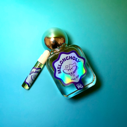 A small clear glass perfume bottle labeled 'MELONCHOLy' with a metallic silver cap, shown next to a matching sample on a bright turquoise gradient background.
