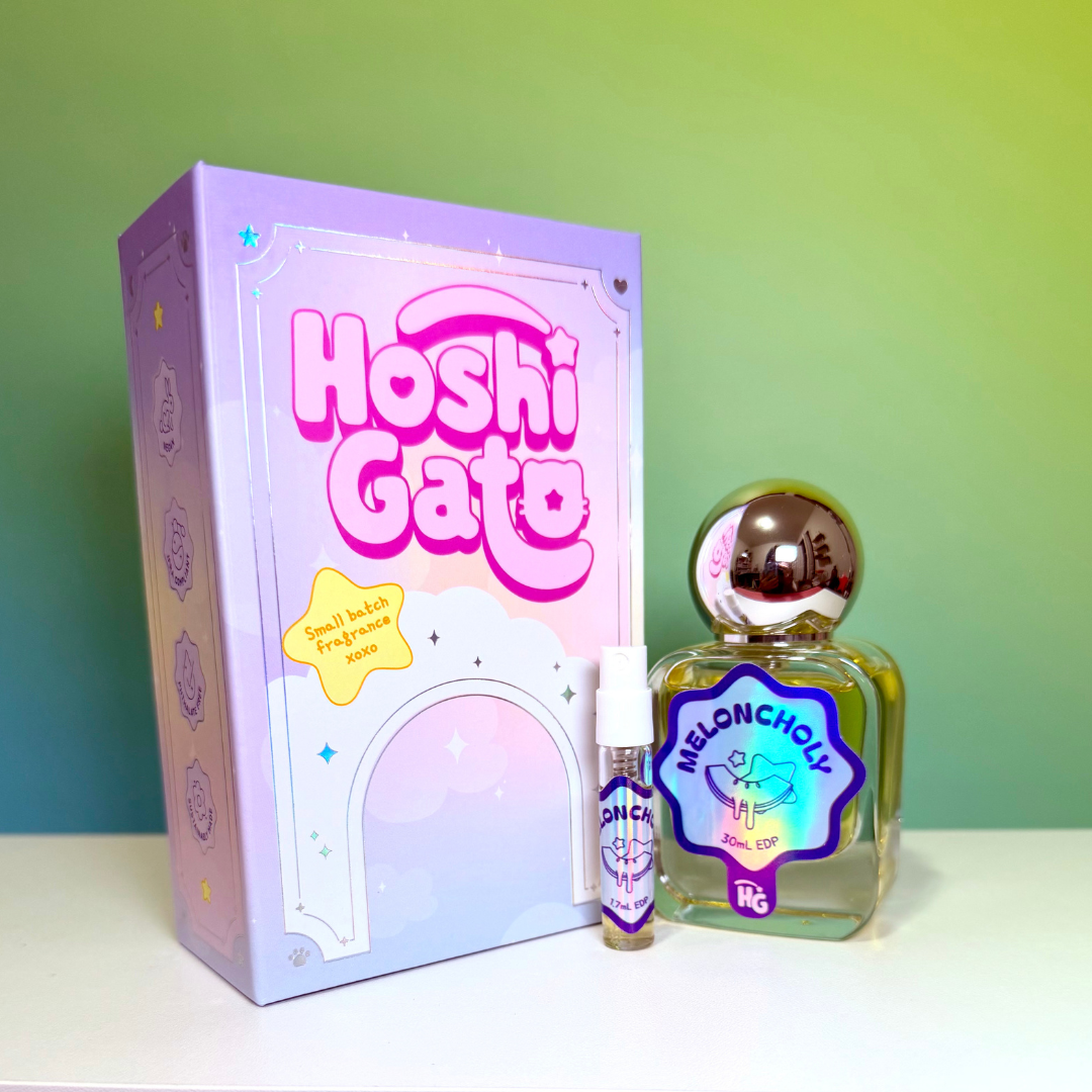 a lavender and pink decorative box, a small sample vial, and a clear glass perfume bottle labelled "meloncholy" with a metallic cap, set against a green gradient background. 
