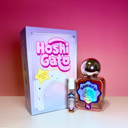 a lavender and pink box, clear glass bottle of Rainbow Perfume with spherical silver cap, and a matching sample vial on a pink gradient background.
