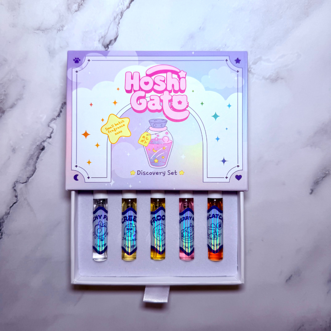 Hoshi Gato Discovery Set perfume spray vials in a decorative purple box, displayed on a light gray marble surface.