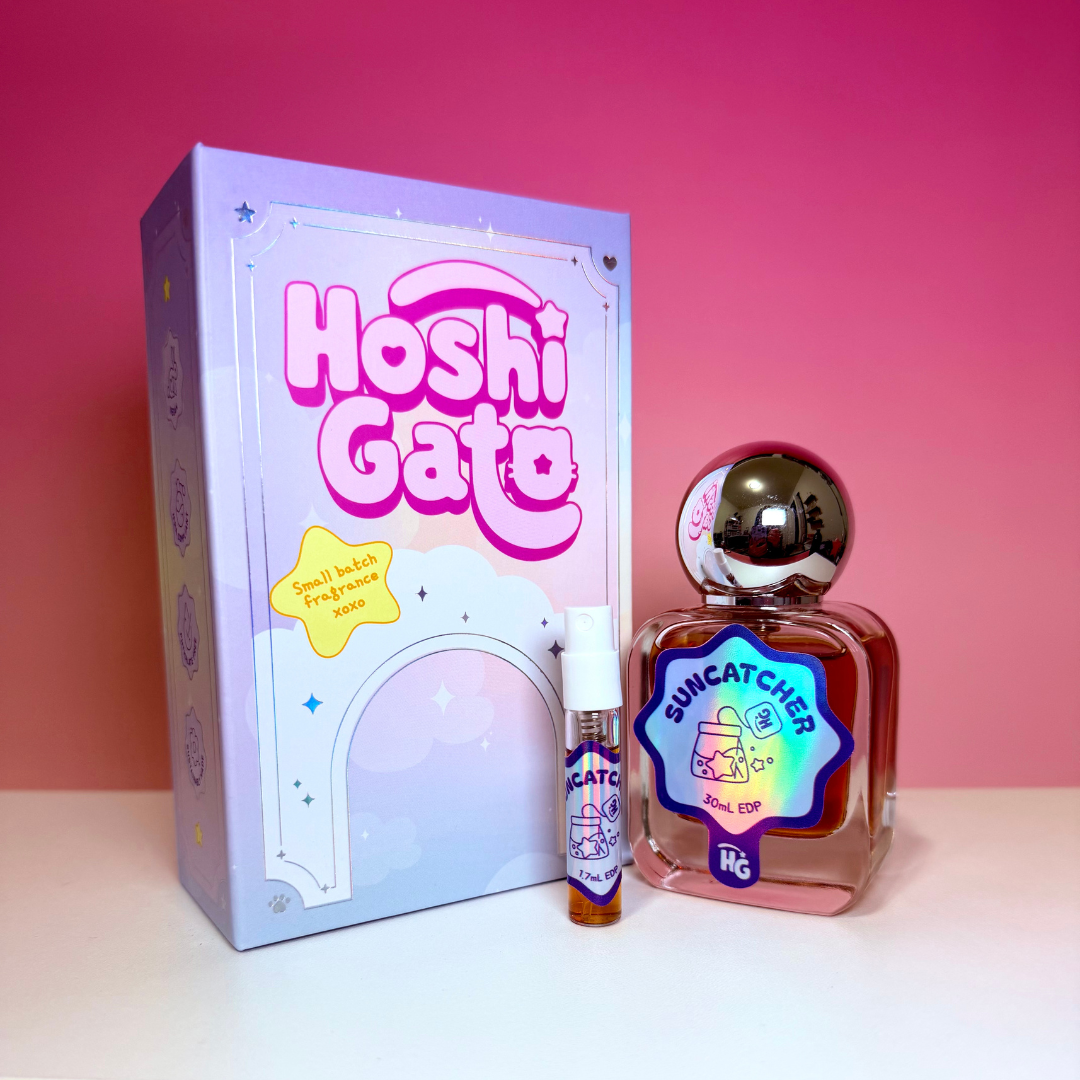 a pastel purple and pink outer box, a small sample spray vial, and a larger rectangular bottle of suncatcher perfume with a reflective silver cap, all set against a pink gradient background.